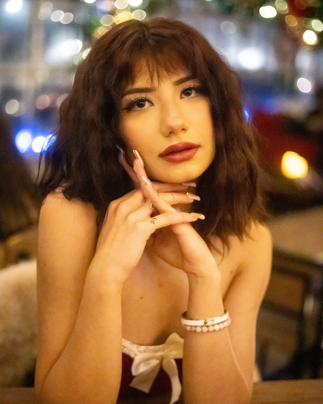 Asal Dabbaghchian resting her chin on her hands at a cafe table, holiday lights softly blurred behind her